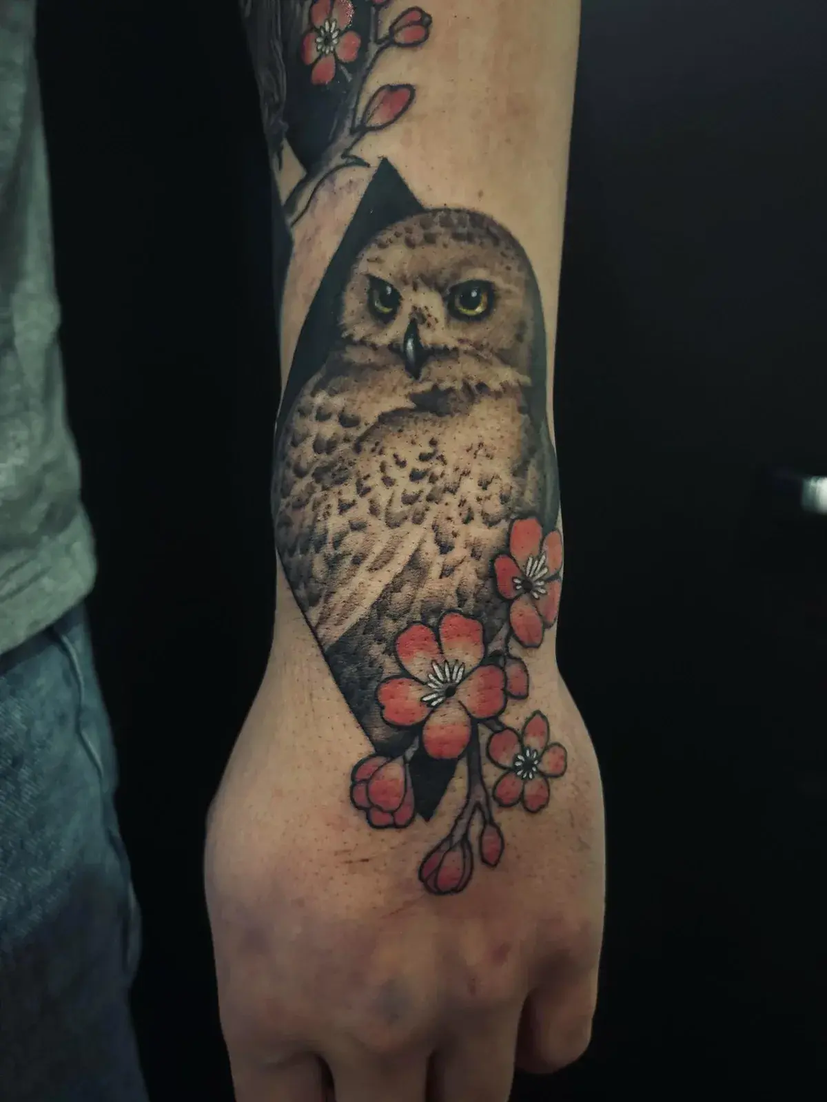 Tatouage d'un harfang et de fleurs de cerisier couvrant une main, réalisé chez ArtCore.