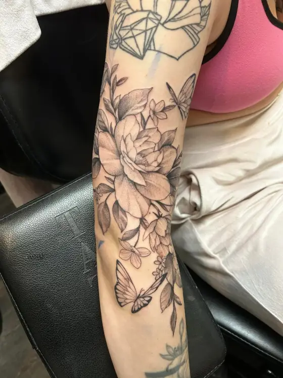 Manchette florale au noir et gris : pivoine, feuillage et papillons sur un avant-bras.