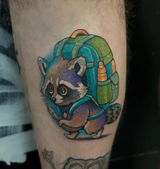 Tatouage couleur d'un raton laveur portant un sac à dos, sur un mollet.