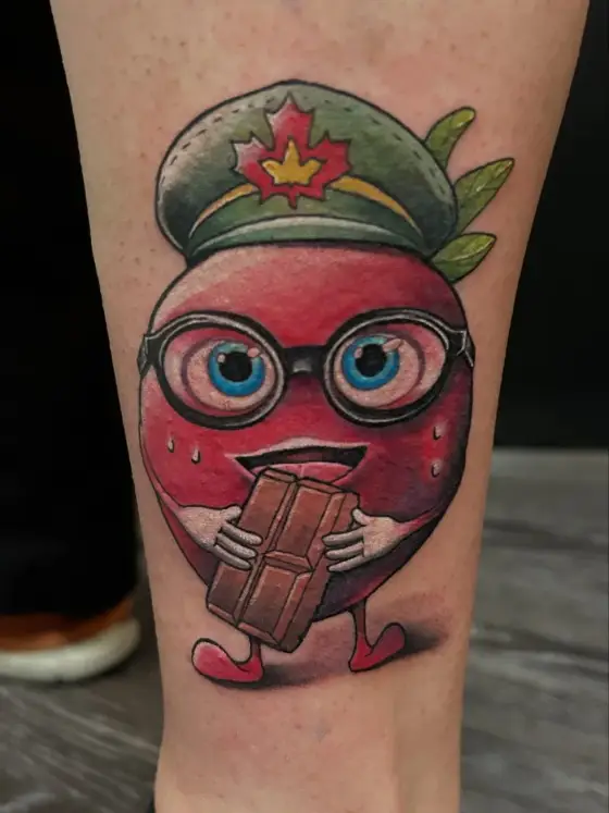 Tatouage couleur d'une fraise à lunettes coiffée d'une casquette, croquant une tablette de chocolat.